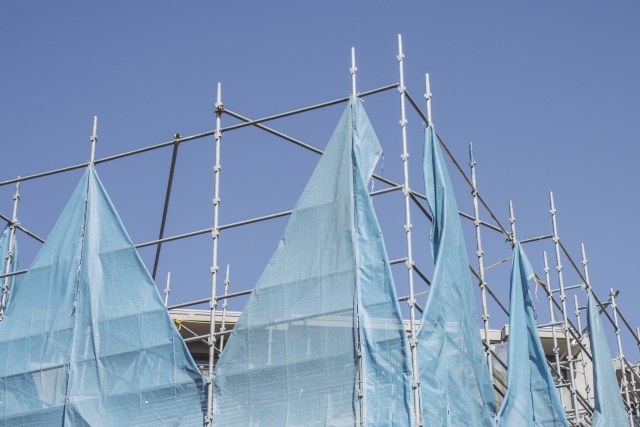 八尾市で屋根修理を行う住宅。足場と青い養生シートで囲われた屋根工事現場